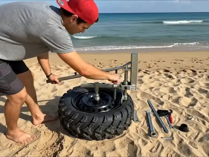 A person using an LCTX tire changer on a wheel at the beach